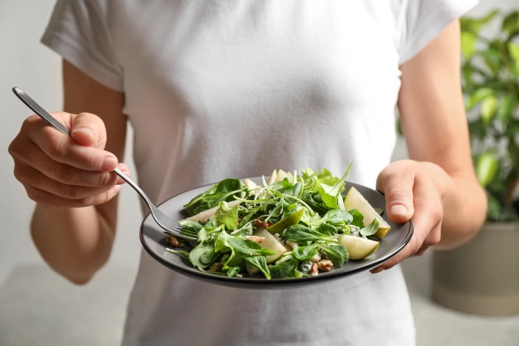 A person eating a spinach and pear salad on a plate.