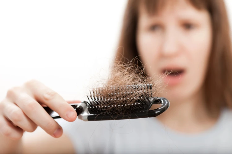 A woman looking at a clump of hair in her hairbrush.