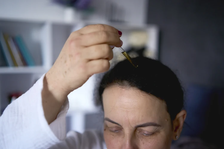A woman uses a topical oil for hair health.