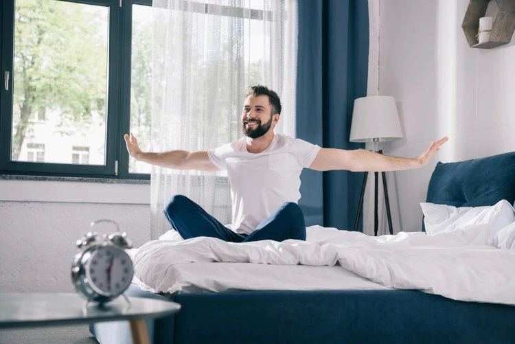 A man waking up and stretching in bed.