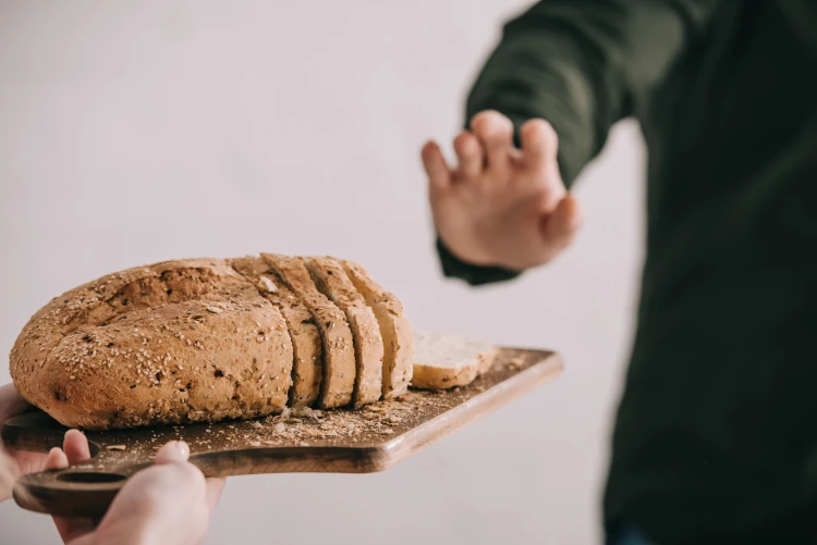 A person holding their hand up to reject the offer of a slice of bread.